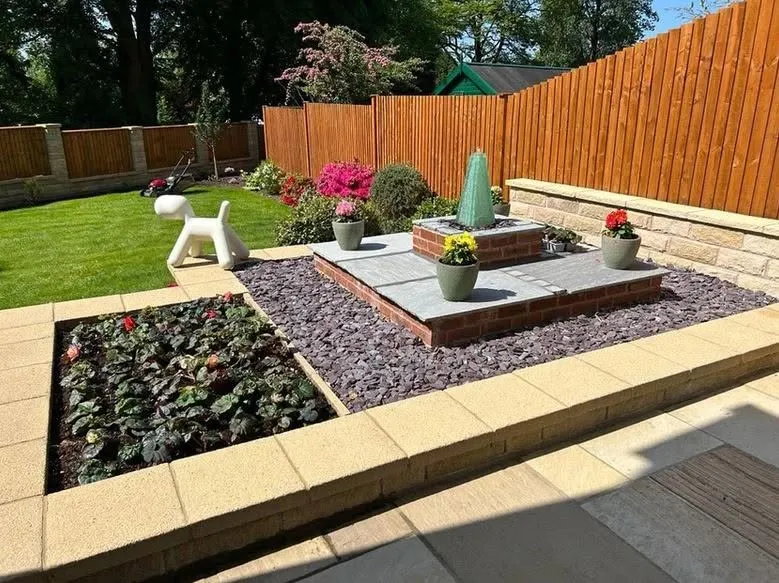 A landscaped garden with a raised stone patio, a brick water feature and potted flowers